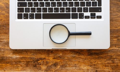 Magnifying glass on a computer laptop, wooden office desk background, top view. Search, SEO concept